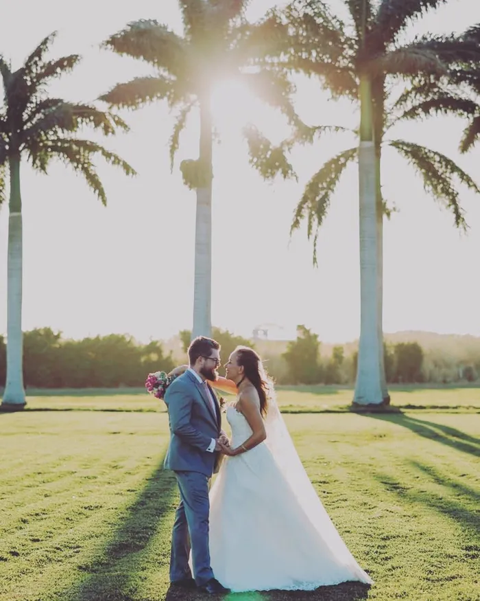 Pareja abrazada entre palmeras altas con el sol de la tarde detrás