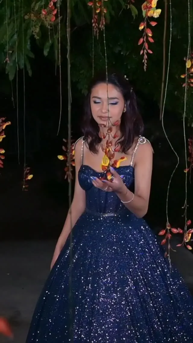 Quinceañera con vestido azul brillante, de noche, entre flores colgantes